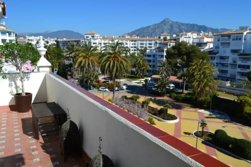 Marbella apartment terrace overlooking palm trees, coastal buildings, and mountain views in Puerto Banús