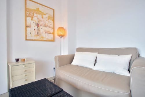 Bright bedroom in Marbella Home Rentals apartment with beige sofa, white pillows, wooden nightstand, and framed art in Puerto