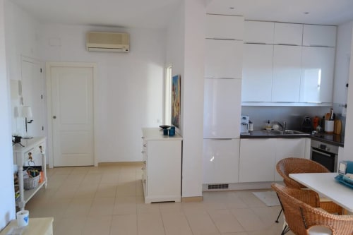 Modern open-plan kitchen and dining area in Marbella seaview apartment with white cabinetry and wicker chairs