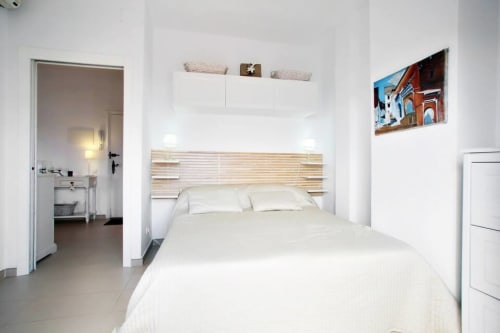 Modern bedroom in Marbella Home Rentals apartment with white bedding, wooden headboard, ensuite bathroom, and coastal decor