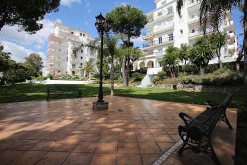 Marbella apartment courtyard with terrace, palm trees, bench, and modern white buildings in Puerto Banús