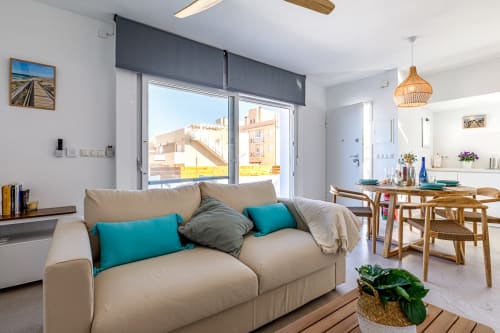 Luminoso salón moderno en San Pedro del Pinatar con sofá beige, cojines turquesas y balcón con vistas