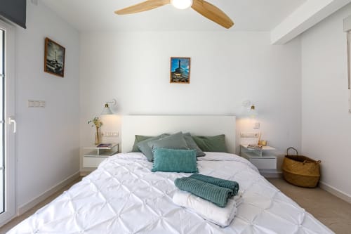 Dormitorio moderno en Haus Holiday Homes de San Pedro del Pinatar con ropa de cama blanca, acentos verdes, ventilador de techo y cuadro enmarcado