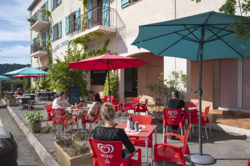 Terrasse extérieure de l'Hôtel Restaurant Le Verdon avec chaises rouges et parasols colorés surplombant Les Salles sur Verdon