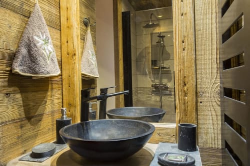 Salle de bains luxueuse à Zoppas Courchevel avec vasques en pierre sombre, accents bois et équipements de douche modernes