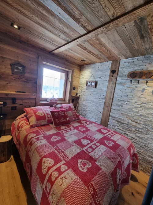 Chambre chaleureuse du chalet Zoppas Courchevel avec literie à motifs rouges, plafond boisé et mur en pierre.