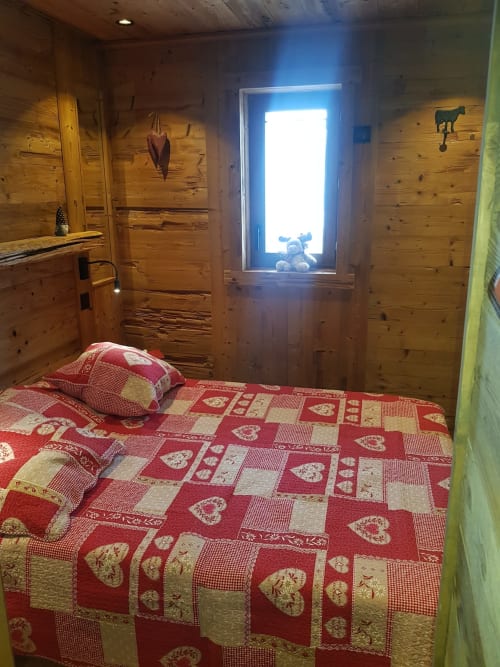 Chambre cosy en bois avec courtepointe rouge patchwork, porte ouverte montrant jouet en peluche, murs en sapin rustique aux Zoppas Courchevel
