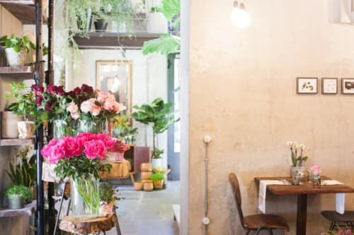 Alessia's Place Como: bright interior with vibrant flowers, plants, wooden table, and modern minimalist design