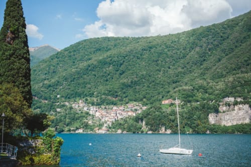 Sailboat on Lake Como with tree-lined mountains and Italian village nestled on hillside, Alessia's Place, Como