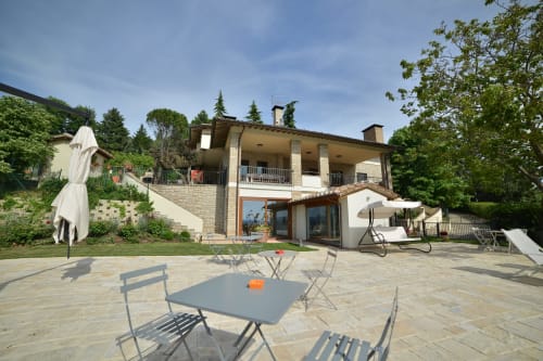 Terrazza esterna della Proprietà Clara ad Assisi con mobili da giardino, ombrelloni e villa in pietra moderna