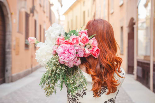 Donna con capelli rossi che tiene peonie rosa e bianche in una suggestiva strada acciottolata a Como, Italia, vicino a Alessia's Place B&B