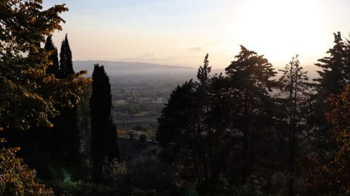 Veduta della valle toscana da Proprietà Clara ad Assisi con cipressi e montagne nebbiose al tramonto