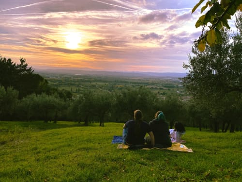 Due ospiti assaporano un picnic al tramonto con vista sulla campagna toscana dalla Proprietà Clara ad Assisi, Italia