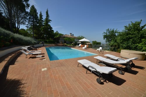 Terrazza in riva alla piscina di Proprietà Clara ad Assisi con lettini, piscina azzurra immacolata e villa toscana sullo sfondo