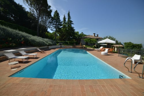 Piscina della Proprietà Clara ad Assisi con lettini, terrazza in terracotta e vista sulla campagna toscana