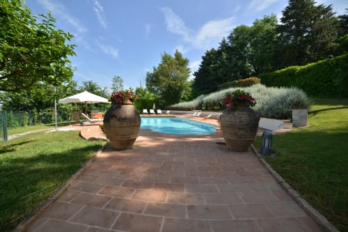 Area piscina di Proprietà Clara ad Assisi con percorso in cotto, vasi decorativi, lettini e giardini curati