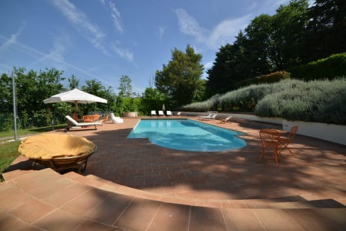 Area piscina di Proprietà Clara ad Assisi con patio in cotto, lettini, ombrellone e vegetazione rigogliosa