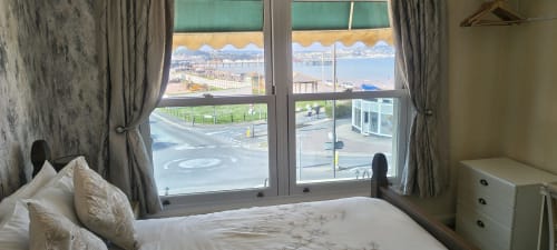 Double bedroom at The Sands Hotel Paignton with sea view, bed with white pillows, grey curtains, and coastal outlook