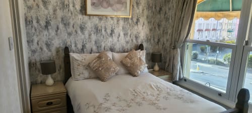 Cozy double bedroom at The Sands Hotel, Paignton with sea view, decorative pillows, and patterned wallpaper