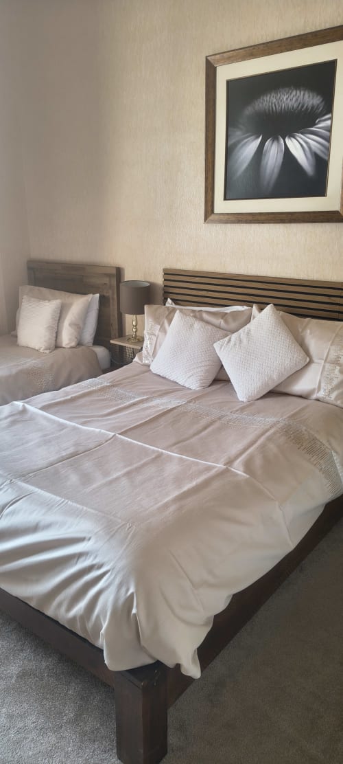 Modern triple bedroom at The Sands Hotel with cream bedding, wooden furniture, and framed floral artwork