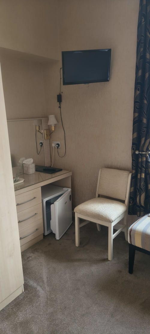 Hotel room corner at The Sands Hotel with wall-mounted TV, desk, chair, and mini fridge in Paignton
