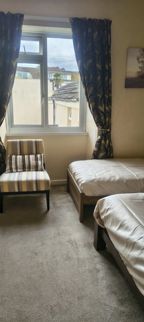 Triple room at The Sands Hotel in Paignton with two beds, striped chair, blue patterned curtains, and window overlooking