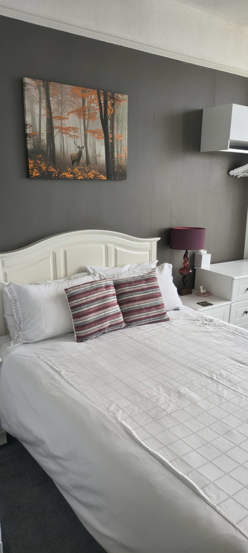 Deluxe double bedroom at The Sands Hotel Paignton with white headboard, striped cushions, and autumn forest artwork on gray