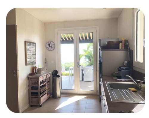 Cucina moderna con vista sul mare nella villa di Porticcio. Porte francesi si aprono su un patio con giardino e spazi living all'aperto.
