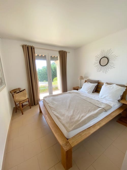 Camera luminosa in villa a Porticcio con letto in legno, cuscini bianchi, vista mare attraverso le porte-finestre e arredi moderni