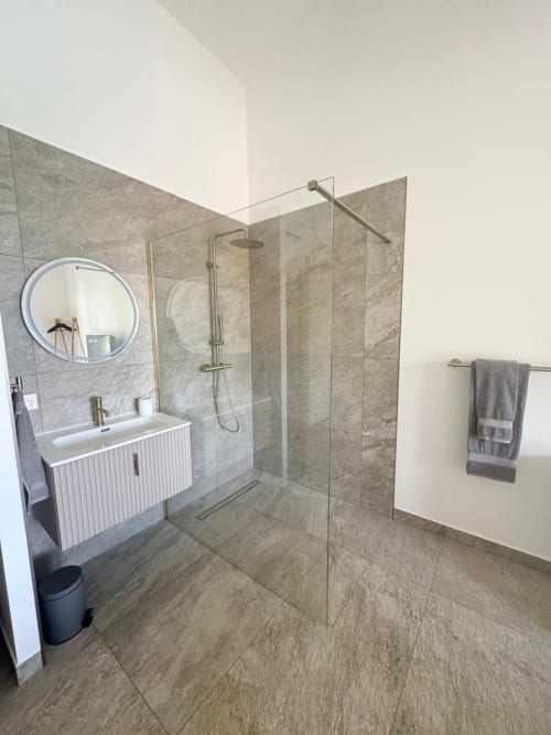 Bagno moderno in villa con vista mare, doccia a pioggia, lavabo bianco, specchio rotondo e scaldasalviette