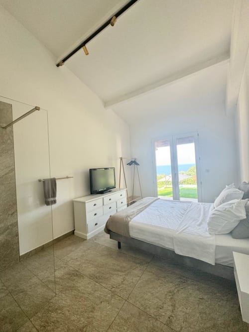 Camera da letto moderna e luminosa con porte vista mare, arredamenti bianchi, TV e bagno ensuite nella villa di Porticcio