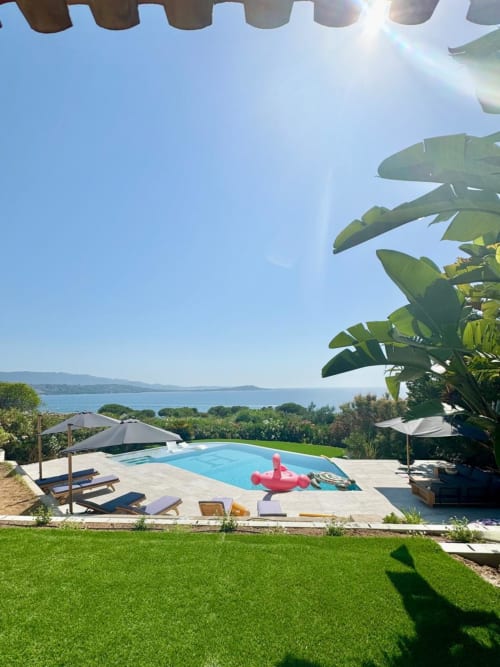 Villa di lusso con piscina a sfioro che affaccia sulla baia di Porticcio, Corsica. Lettini, ombrelloni, piante tropicali e vista mare.