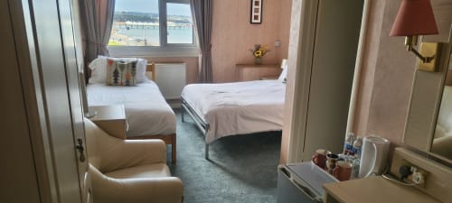 Triple room at The Sands Hotel in Paignton with sea view, two beds, armchair, and coastal scenery visible through window