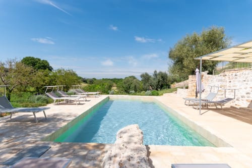Lussuosa piscina a sfioro della villa Trulli Life a Bari, circondata da lettini, terrazze in pietra e ulivi sotto il cielo azzurro