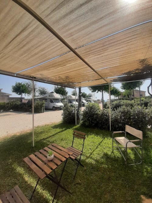 Area esterna ombreggiata del Baia Dorica Camping Village con pod abitativi e tende visibili sullo sfondo
