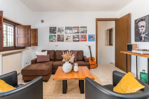 Soggiorno della villa Trullo Il Sassofono presso Trulli Life a Bari con divano marrone, tavolo in legno e chitarra