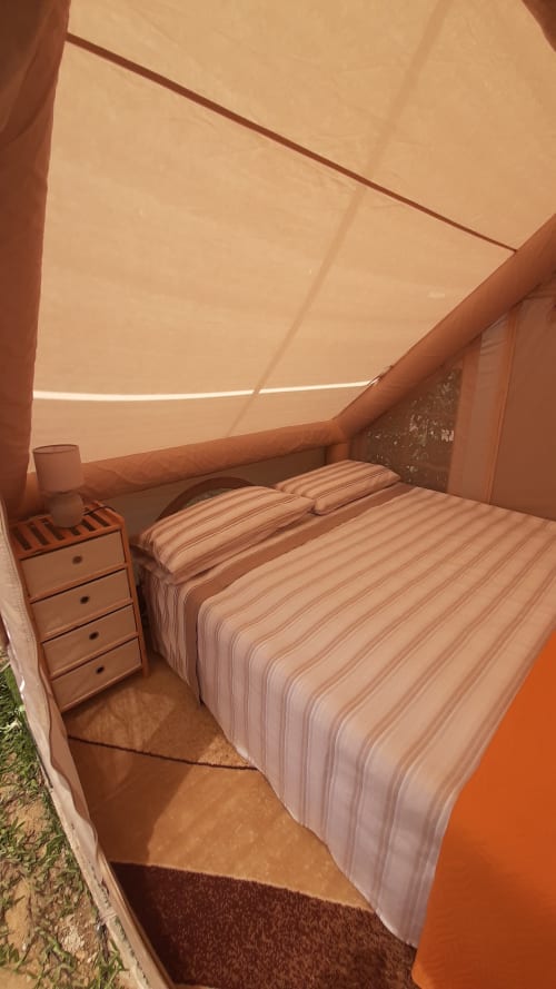 Tente lit double au Baia Dorica Camping Village à Vittoria avec literie rayée, table de nuit et toile beige