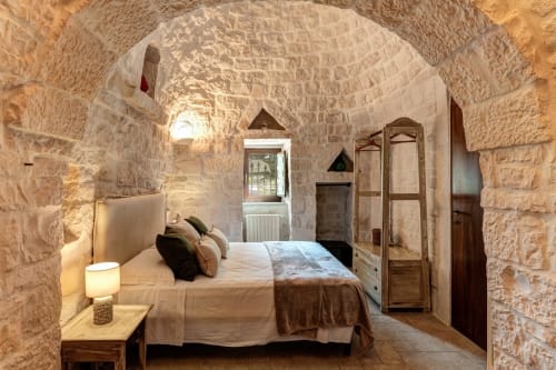 Camera da letto in pietra nella villa Trulli Life, Bari, con soffitto a volta, letto, mobili in legno e vista dalla finestra