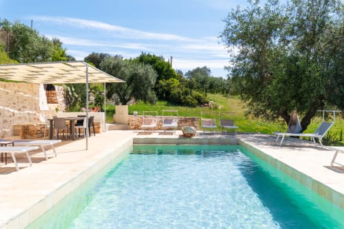 Piscina cristallina della villa Trulli Life a Bari, Italia, con terrazza in pietra, sdraie e uliveti