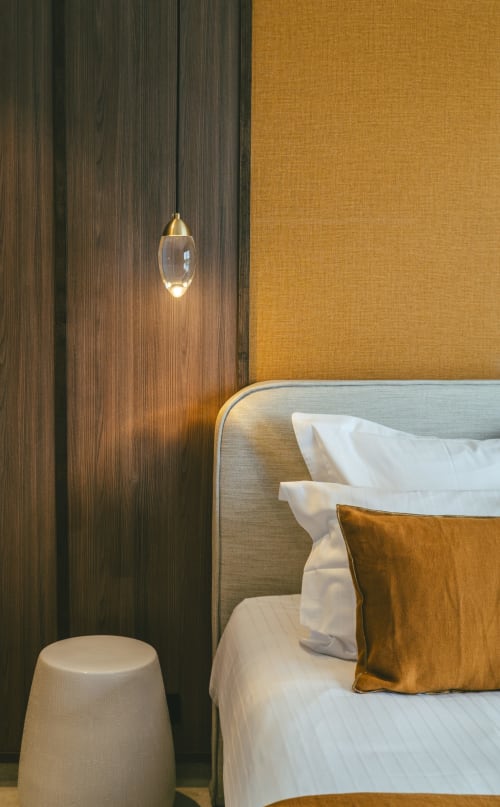Détail de chambre moderne à la Villa Theia : lit, coussin doré, lampe suspendue, mur en bois - Collection Blue Horizon