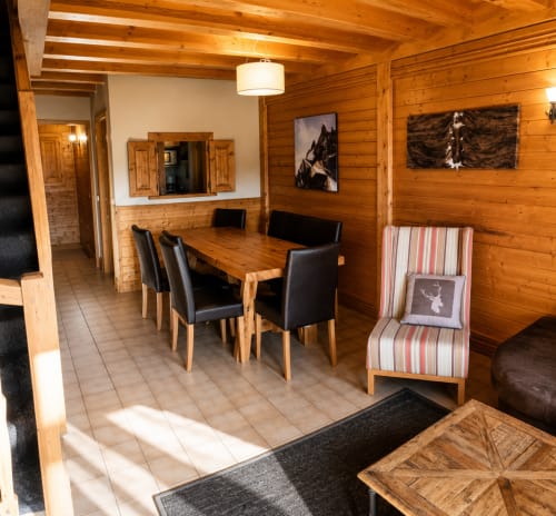 Salle à manger chaleureuse au bois avec table, chaises noires, fauteuil rayé et œuvres de montagne au Chalet des Cimes, Savoie