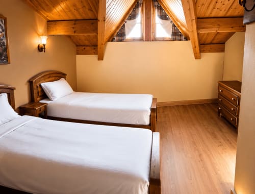 Chambre alpine cosy au Chalet des Cimes en Savoie avec lits jumeaux, poutres en bois et vue sur les montagnes par lucarne
