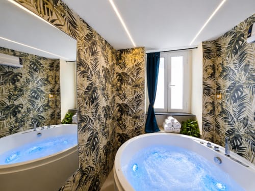 Salle de bain spa luxueux avec deux jacuzzis bleus illuminés, papier peint tropical et vue sur la mer à HomeHolidaySanremo