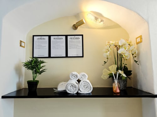Étagère de l'appartement-spa Sanremo avec serviettes roulées, orchidées blanches, plante en pot et informations encadrées sous lumière chaleureuse