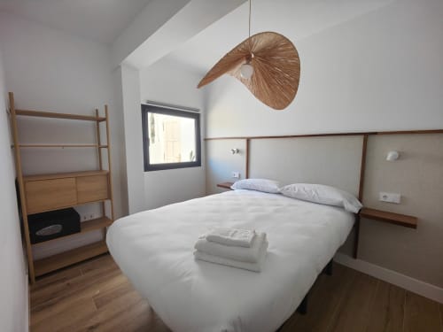 Dormitorio moderno en el apartamento de lujo Nido Anaga en Tenerife con ropa de cama blanca, muebles de madera y lámpara colgante tejida
