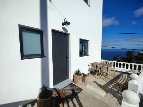 Patio de lujo del apartamento Nido Anaga con vistas al océano, puerta negra, ventanales y zona de estar costera en Tenerife