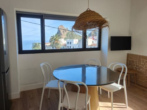 Área de comedor moderna en Nido Anaga con mesa redonda azul, sillas blancas y vistas al océano de las montañas de Santa Cruz de Tenerife