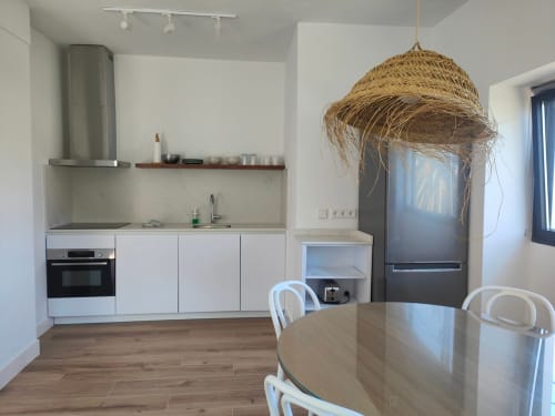 Cocina moderna con muebles blancos, electrodomésticos de acero inoxidable, lámpara colgante tejida y mesa de comedor en Nido Anaga, Tenerife