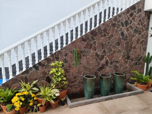 Patio de Nido Anaga en Tenerife con macetas, flores amarillas y vasijas de cerámica verde contra pared de piedra oscura