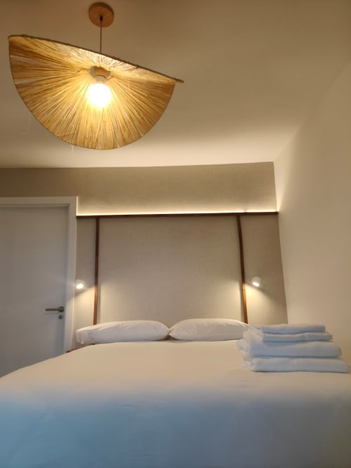 Habitación moderna del hotel Nido Anaga en Tenerife con ropa de cama blanca, cabecero geométrico y luminaria colgante escultórica